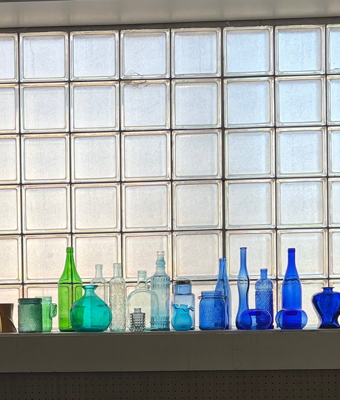 Green and blue glass bottles lined along a backlit glass-block window