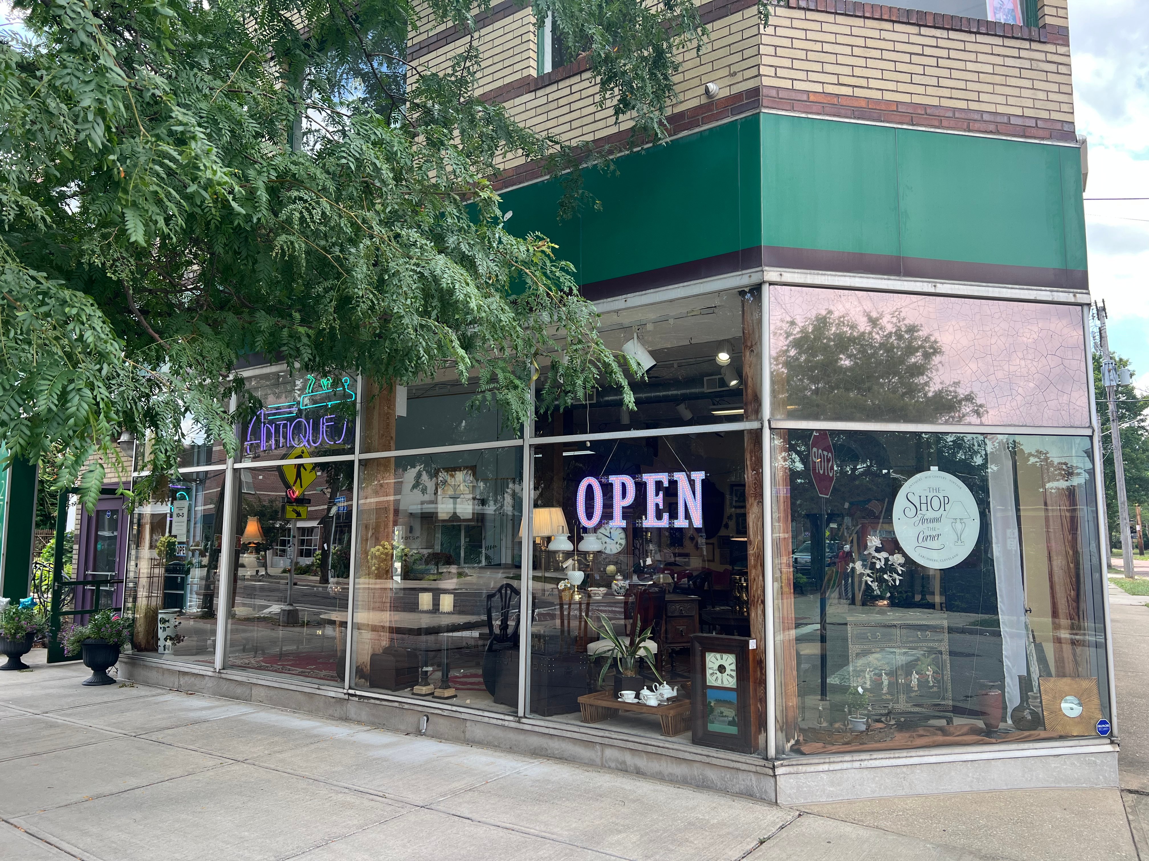 The shop's green corner storefront on Larchmere Boulevard, with a lit OPEN sign and the shop's round badge in the window